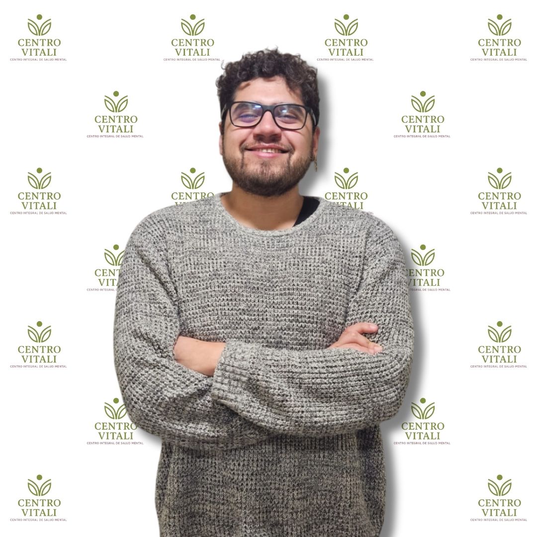 Profesional de salud mental de Centro Vitali, hombre con lentes y sweater gris, brazos cruzados y sonrisa, fondo institucional.
