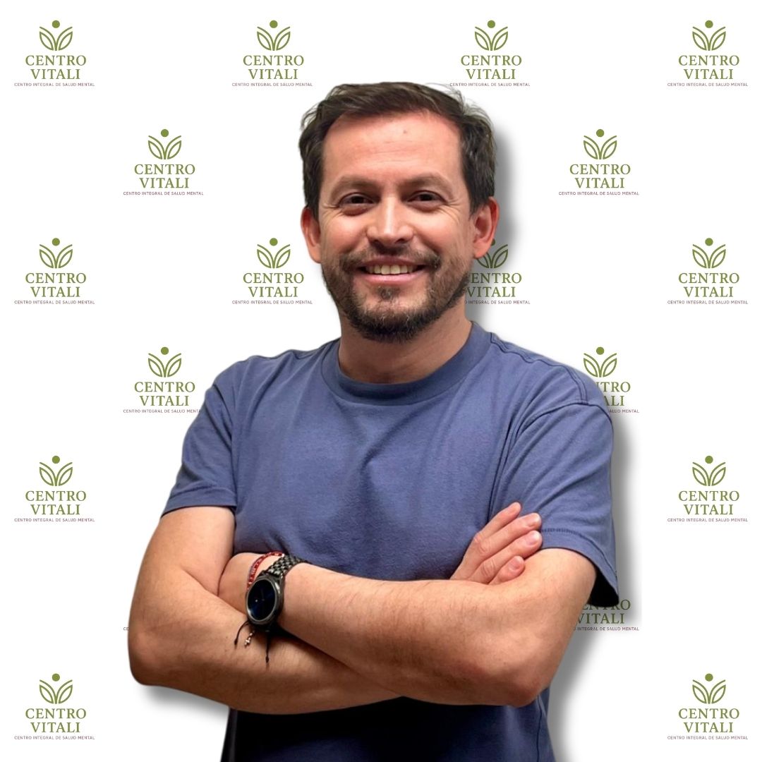 Profesional de salud mental de Centro Vitali, hombre con polera azul y brazos cruzados, sonrisa amable, fondo con logo.