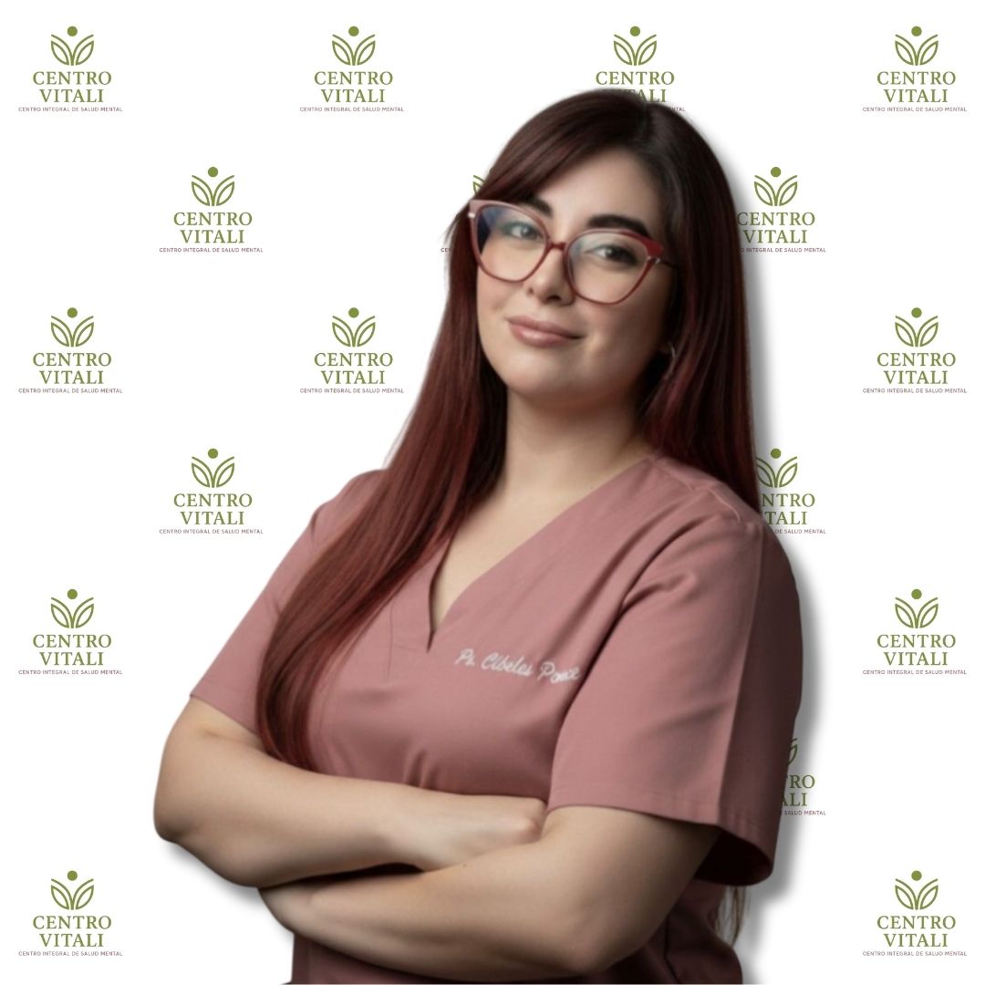 Profesional de salud mental de Centro Vitali, mujer con uniforme rosado y lentes, brazos cruzados, expresión cercana, fondo institucional.